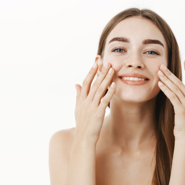 charming-relaxed-gentle-young-woman-making-cosmetological-procedure-applying-facial-cream-face-with-fingers-smiling-broadly-feeling-perfect-taking-care-skin